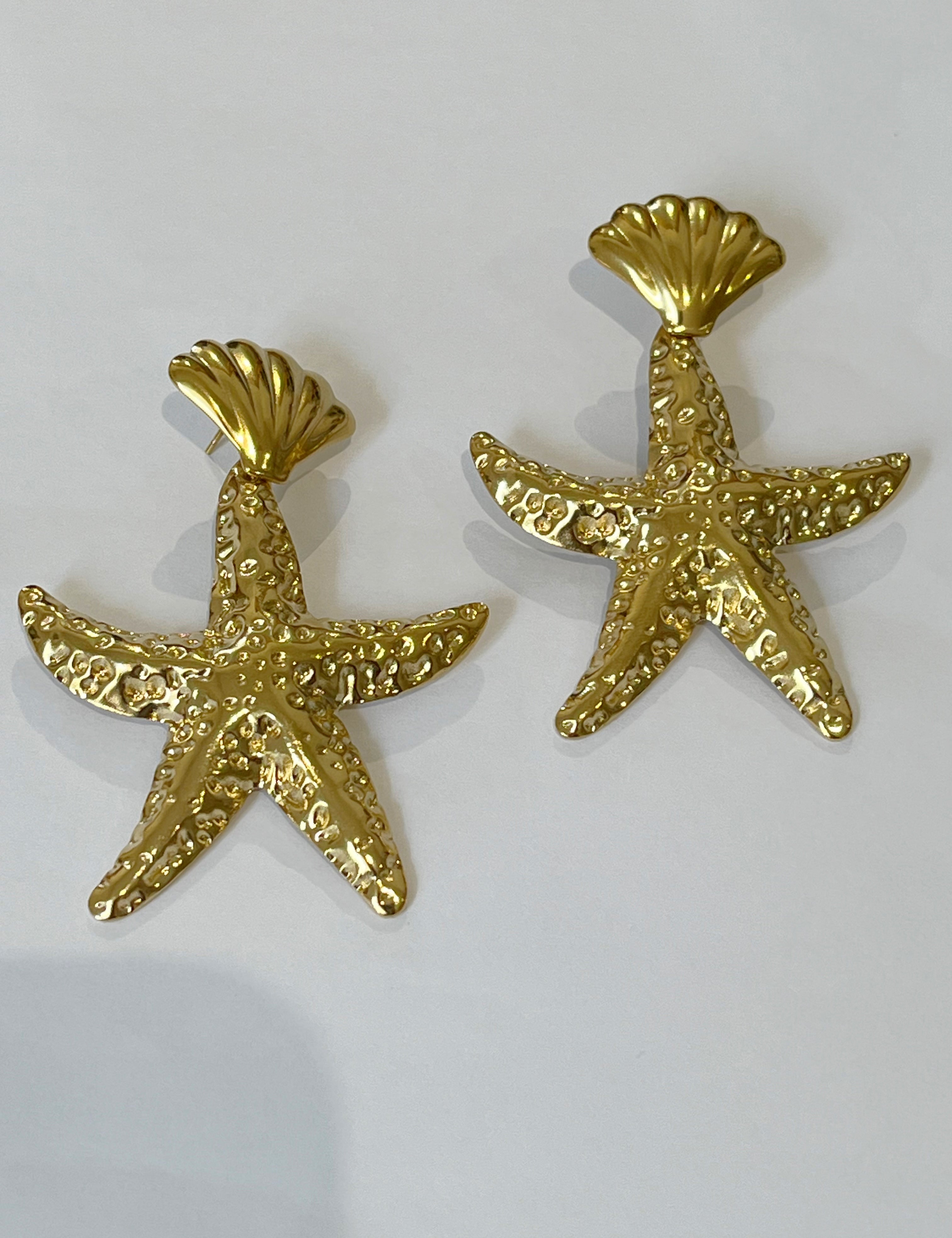 Boucles Étoile de mer dorées texturées suspendues à une puce coquillage, sur fond gris - Ordiajade