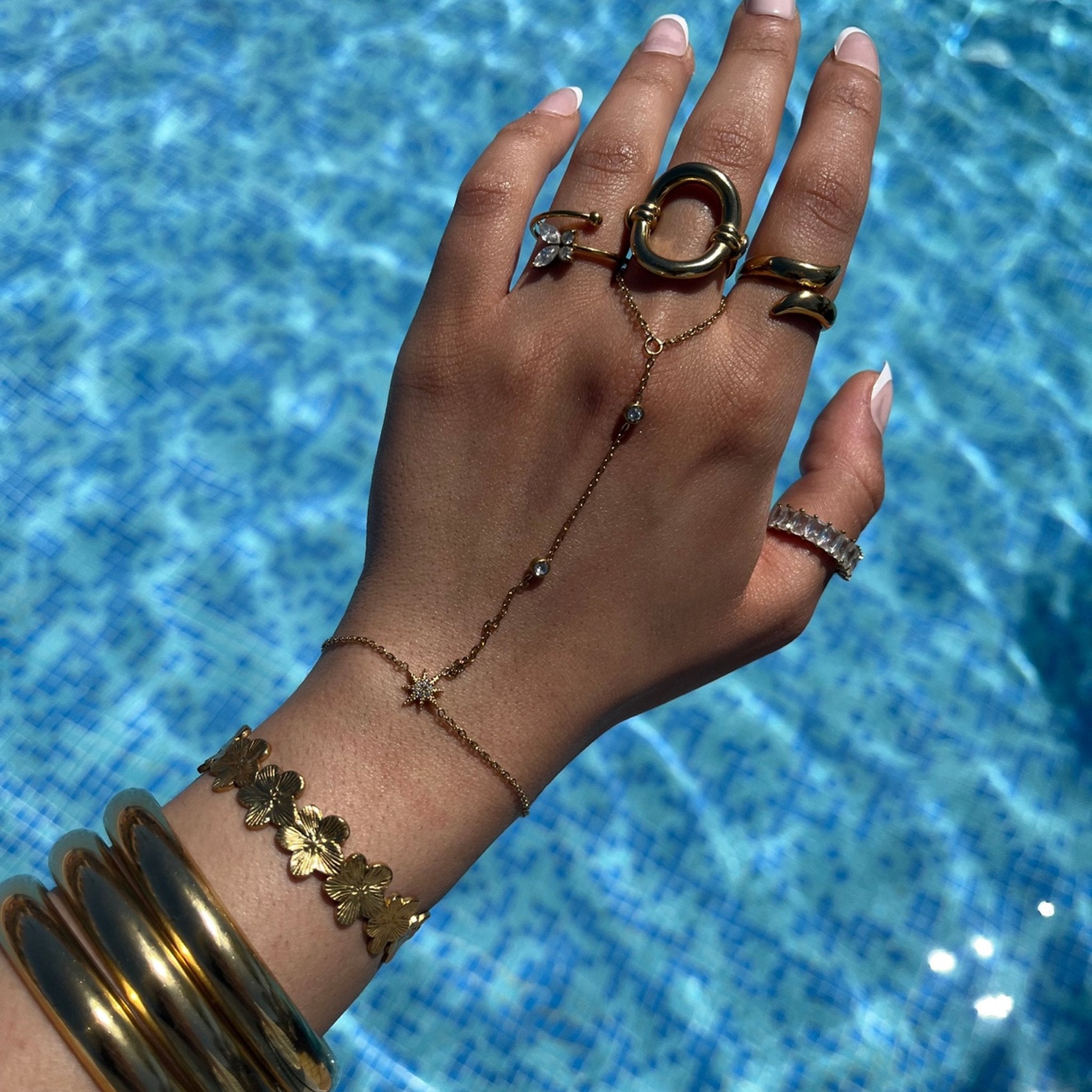 Chaîne de main Mirage portée avec des bagues et bracelets dorés au bord de la piscine - Ordiajade