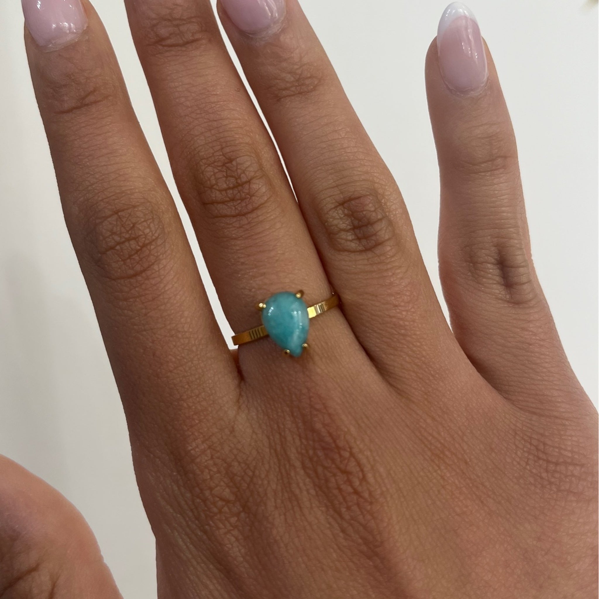 Bague Amablue dorée à pierre bleue en forme de goutte, portée au doigt - Ordiajade