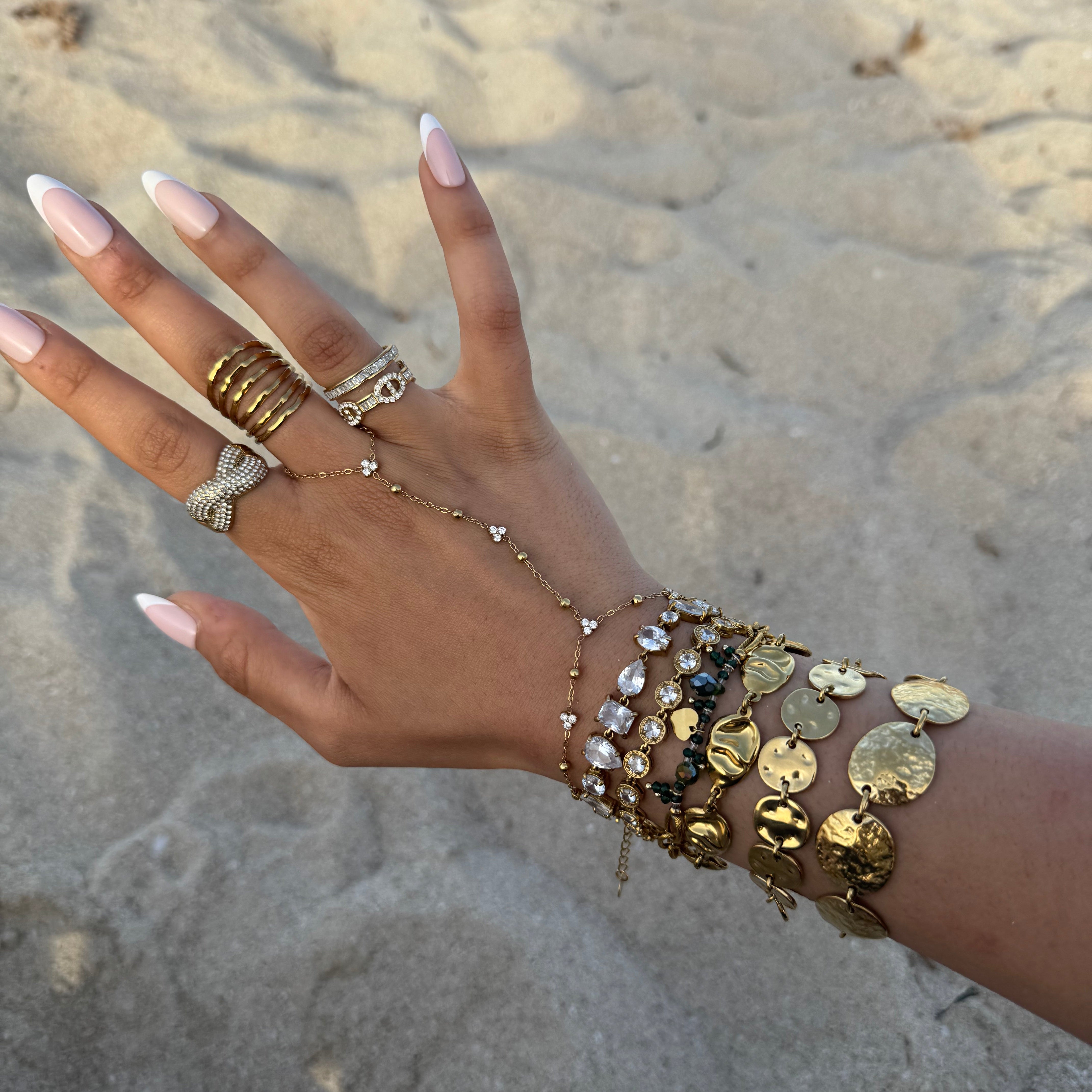 Bague Rym ajustable portée à la main avec d'autres bijoux dorés en bord de mer.