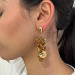 Grandes boucles d'oreilles Rich dorées avec motifs fleurs marron et perles nacrées portées de profil.