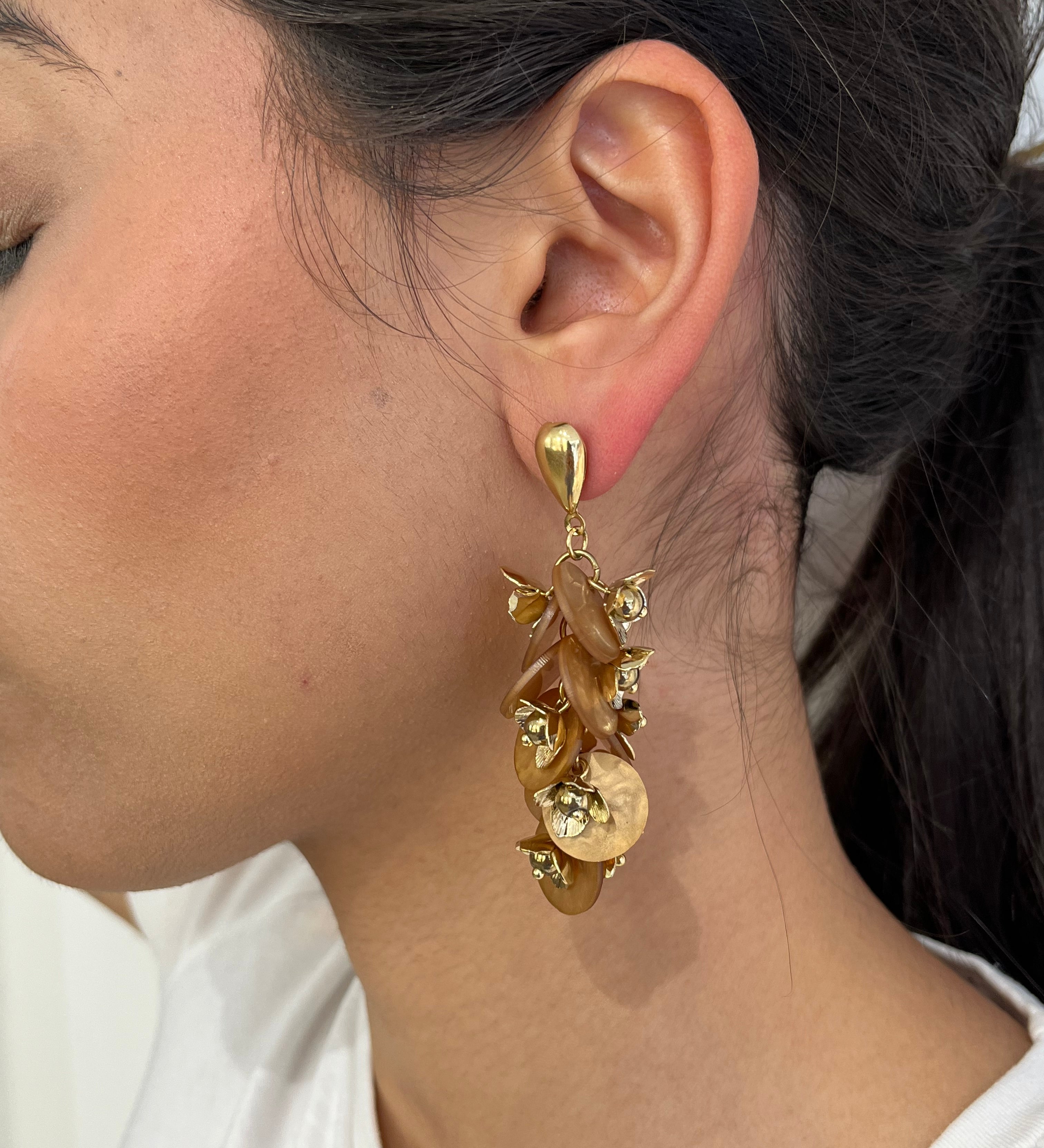 Grandes boucles d'oreilles Rich dorées avec motifs fleurs marron et perles nacrées portées de profil.