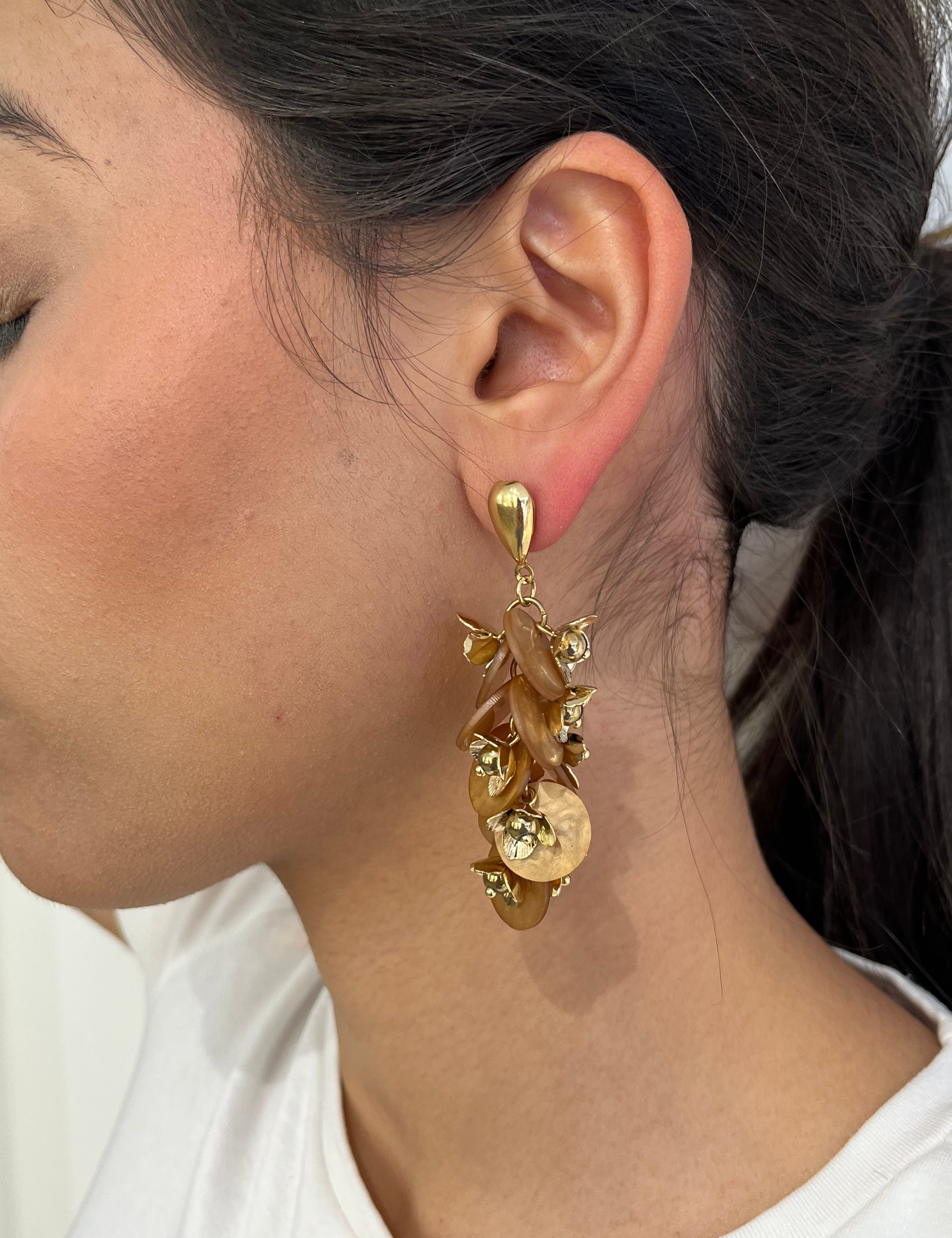 Grandes boucles d'oreilles Rich dorées avec motifs fleurs marron et perles nacrées portées de profil.