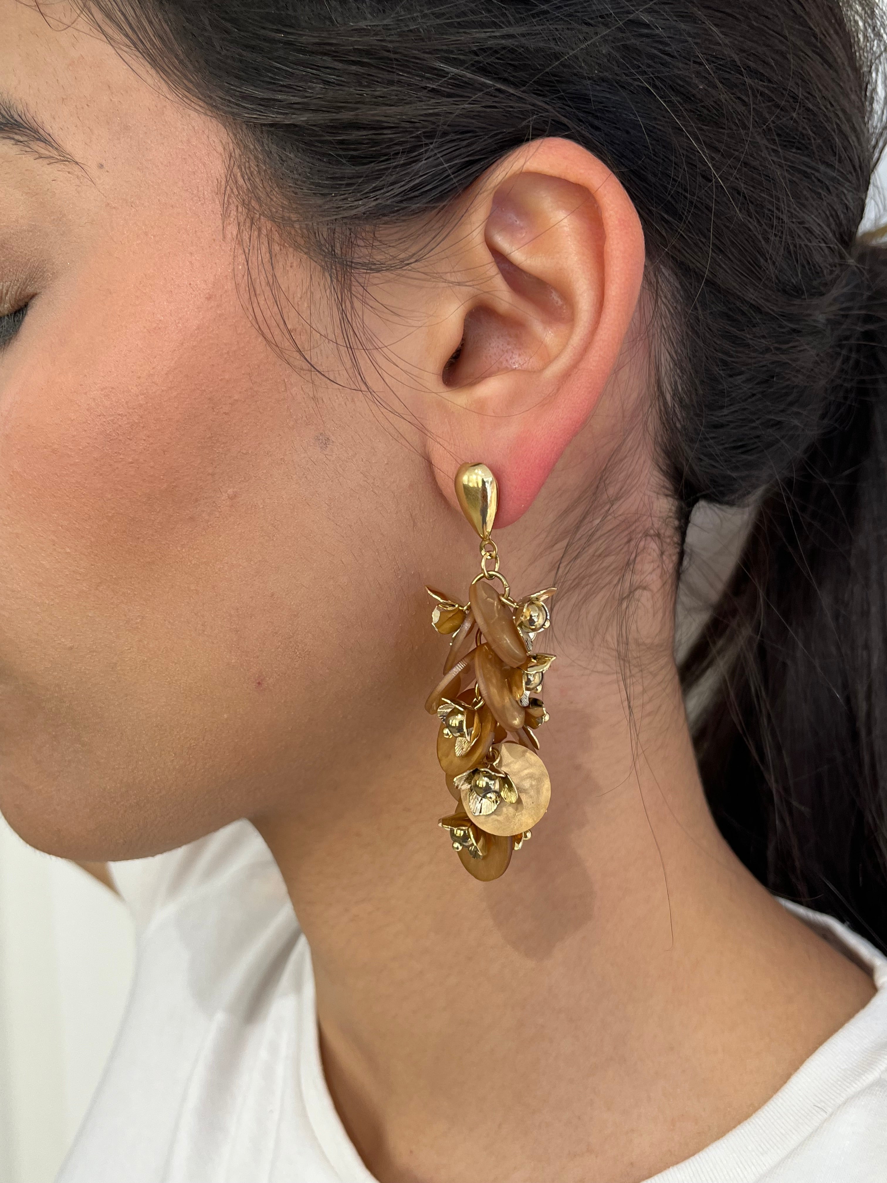 Grandes boucles d'oreilles Rich dorées avec motifs fleurs marron et perles nacrées portées de profil.