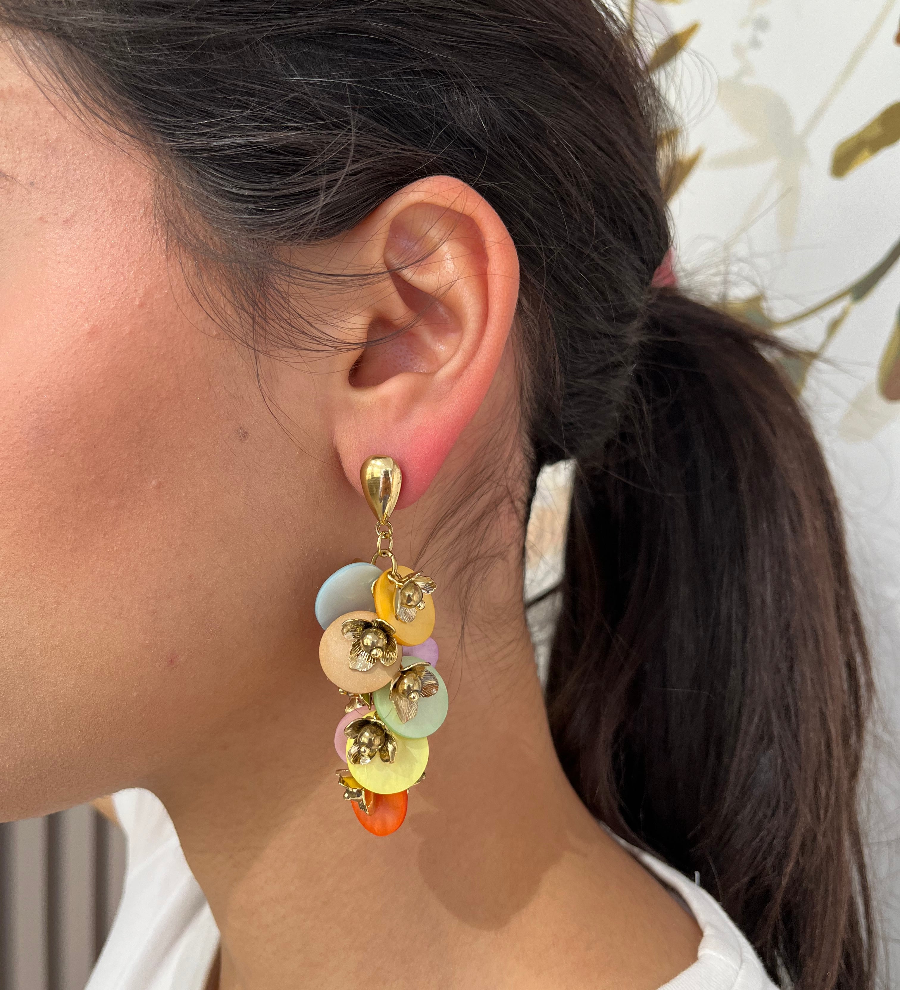 Grandes boucles d'oreilles Rich dorées avec motifs fleurs multicolore et perles nacrées portées de profil.