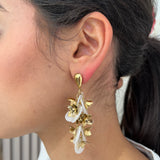 Grandes boucles d'oreilles Rich dorées avec motifs fleurs blanches et perles nacrées portées de profil.