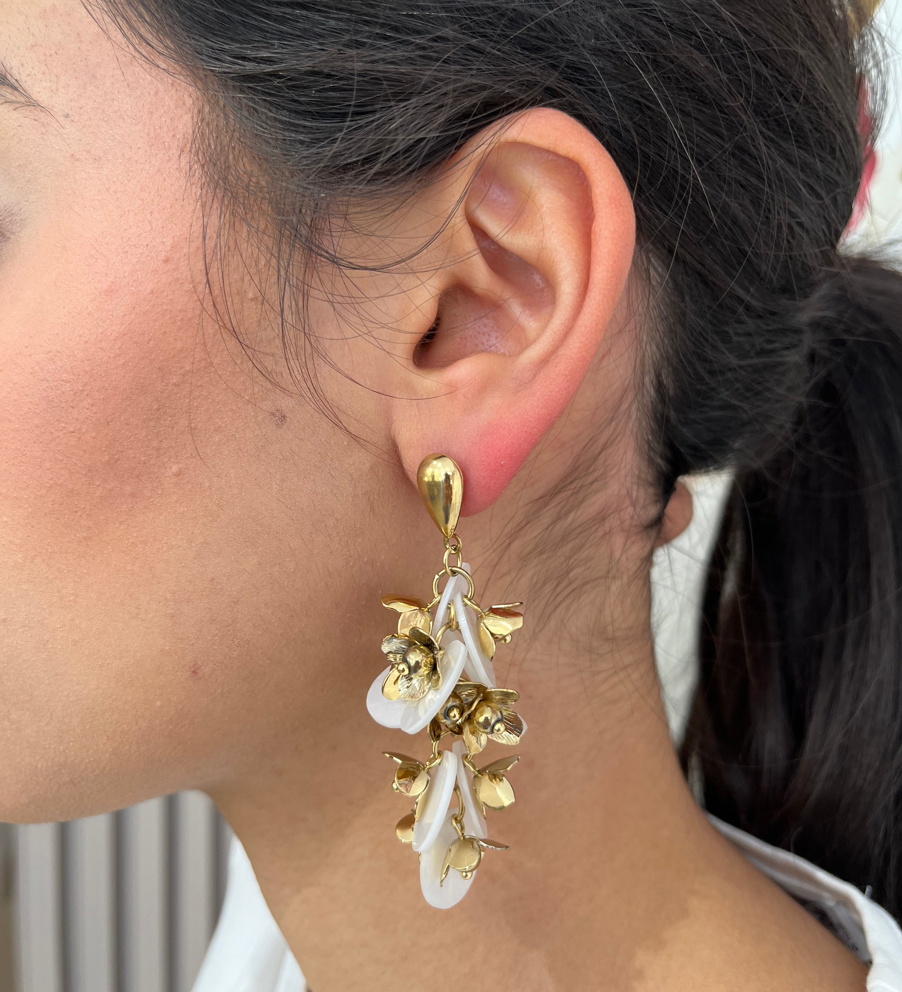 Grandes boucles d'oreilles Rich dorées avec motifs fleurs blanches et perles nacrées portées de profil.