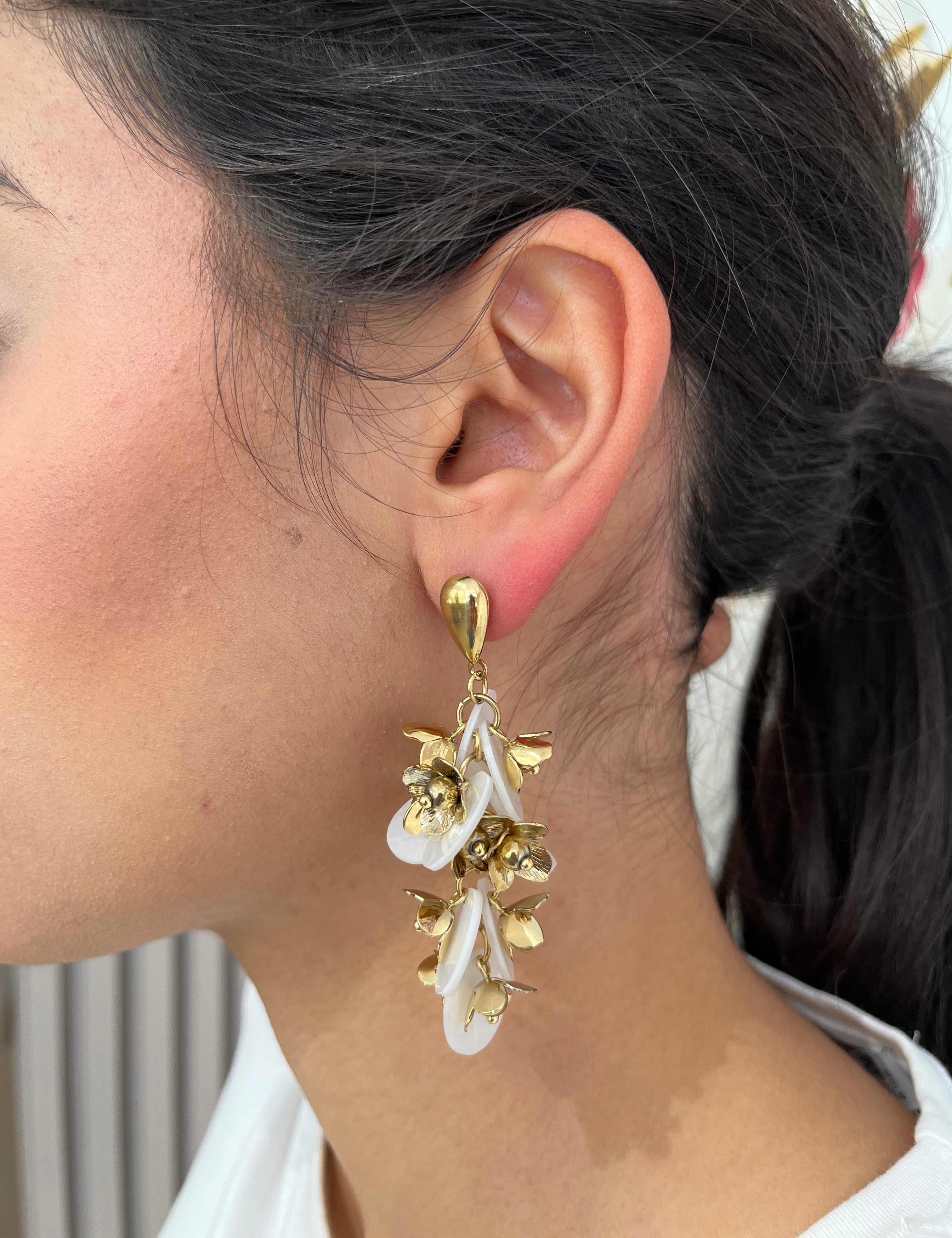 Grandes boucles d'oreilles Rich dorées avec motifs fleurs blanches et perles nacrées portées de profil.