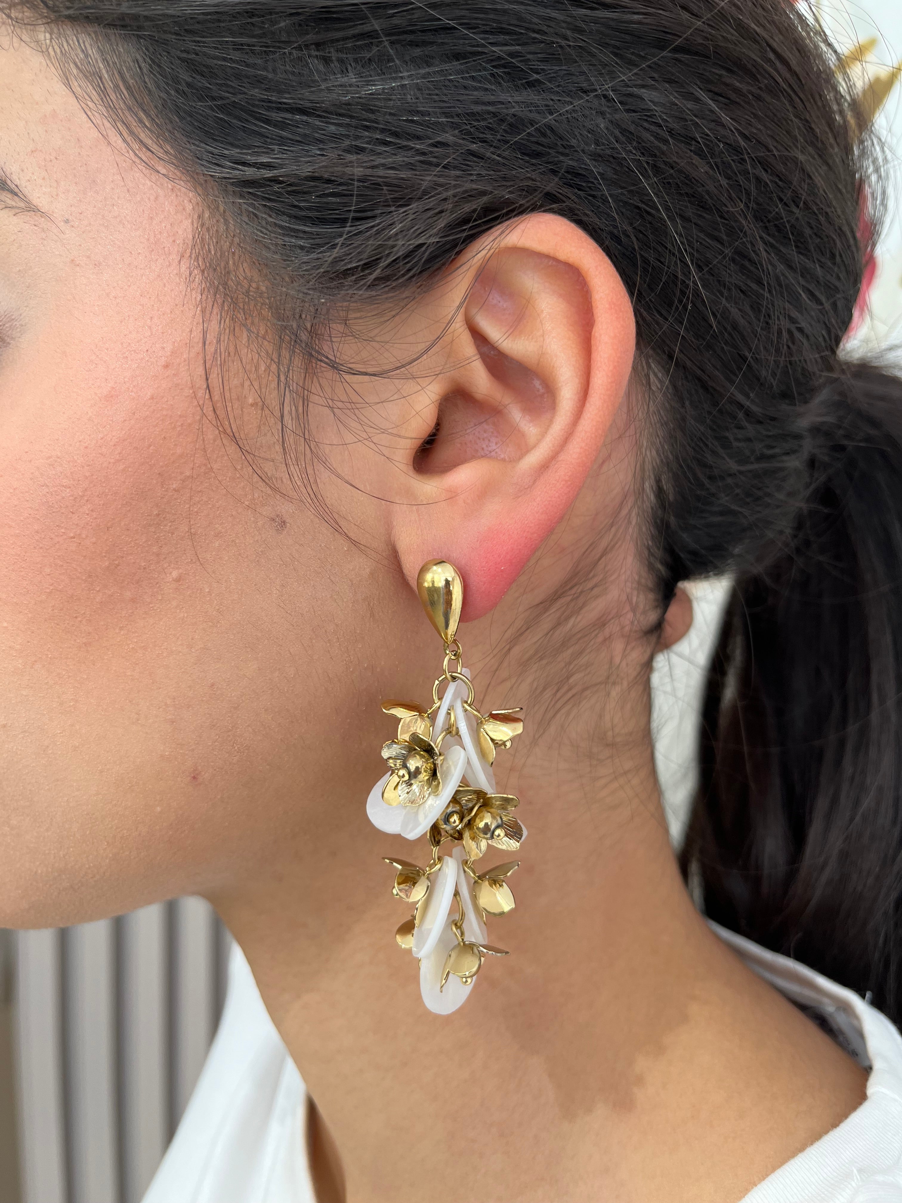 Grandes boucles d'oreilles Rich dorées avec motifs fleurs blanches et perles nacrées portées de profil.