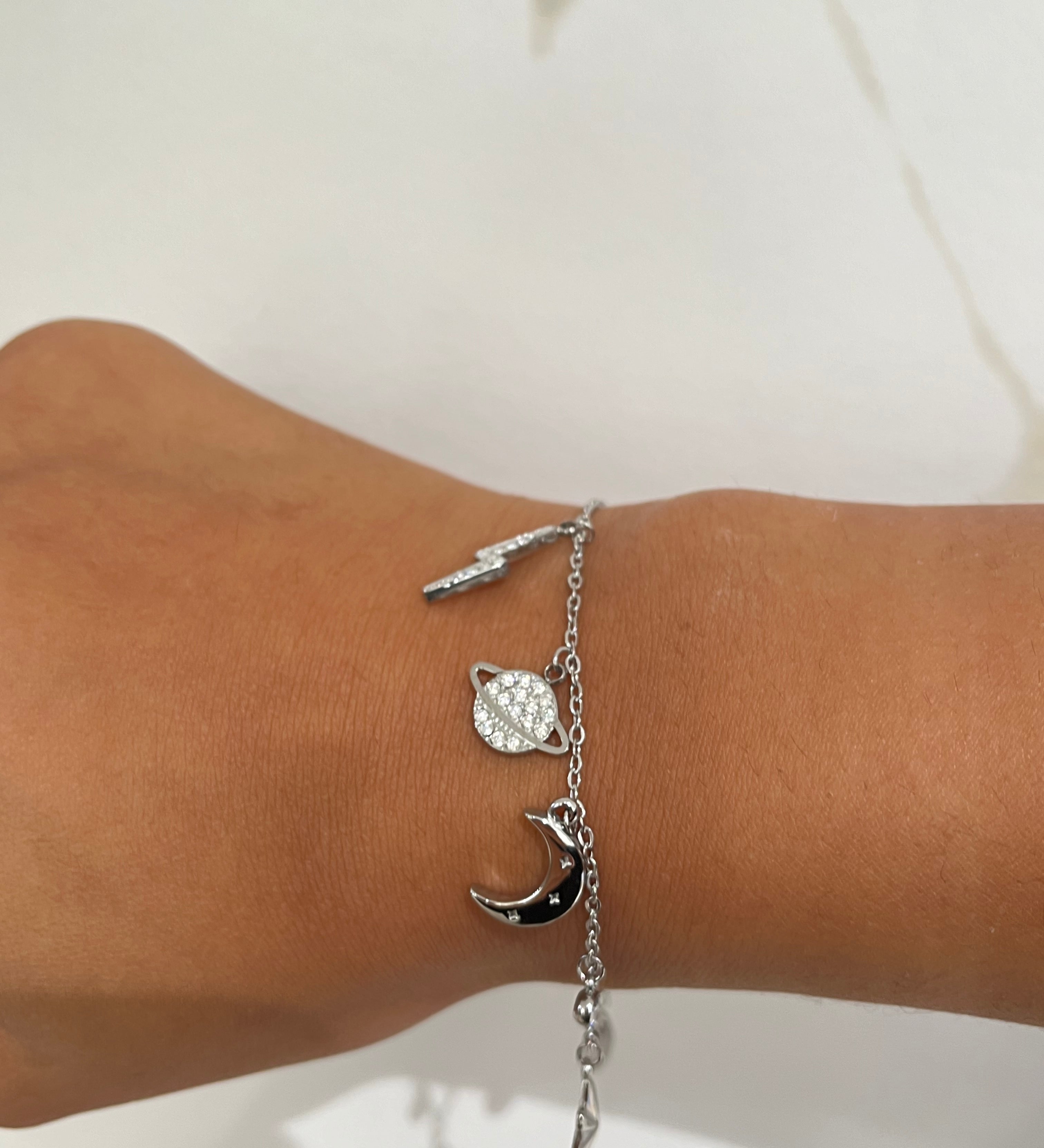 Bracelet argent à maillons fins avec breloques en forme d'éclair, de lune et de planète.
