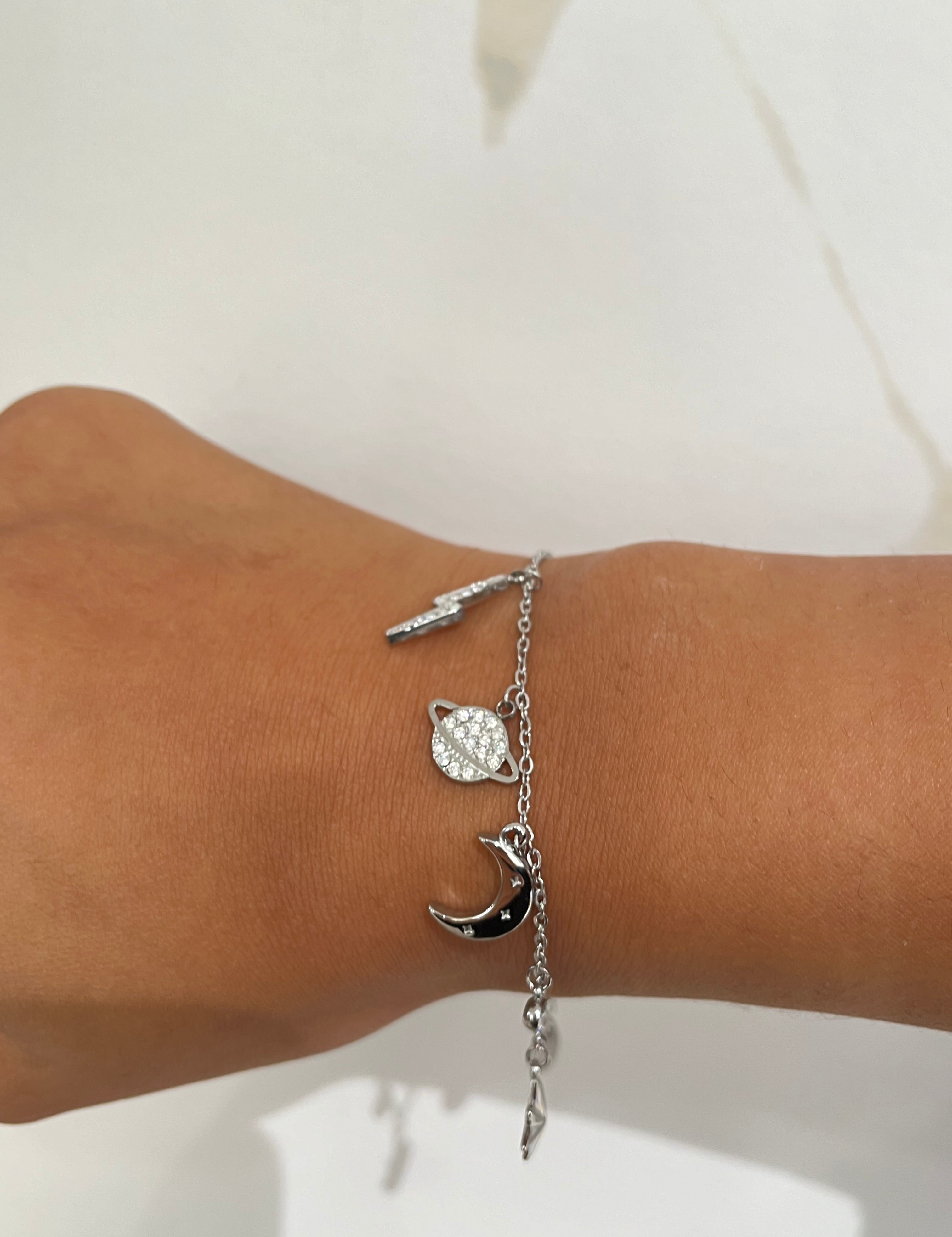 Bracelet argent à maillons fins avec breloques en forme d'éclair, de lune et de planète.