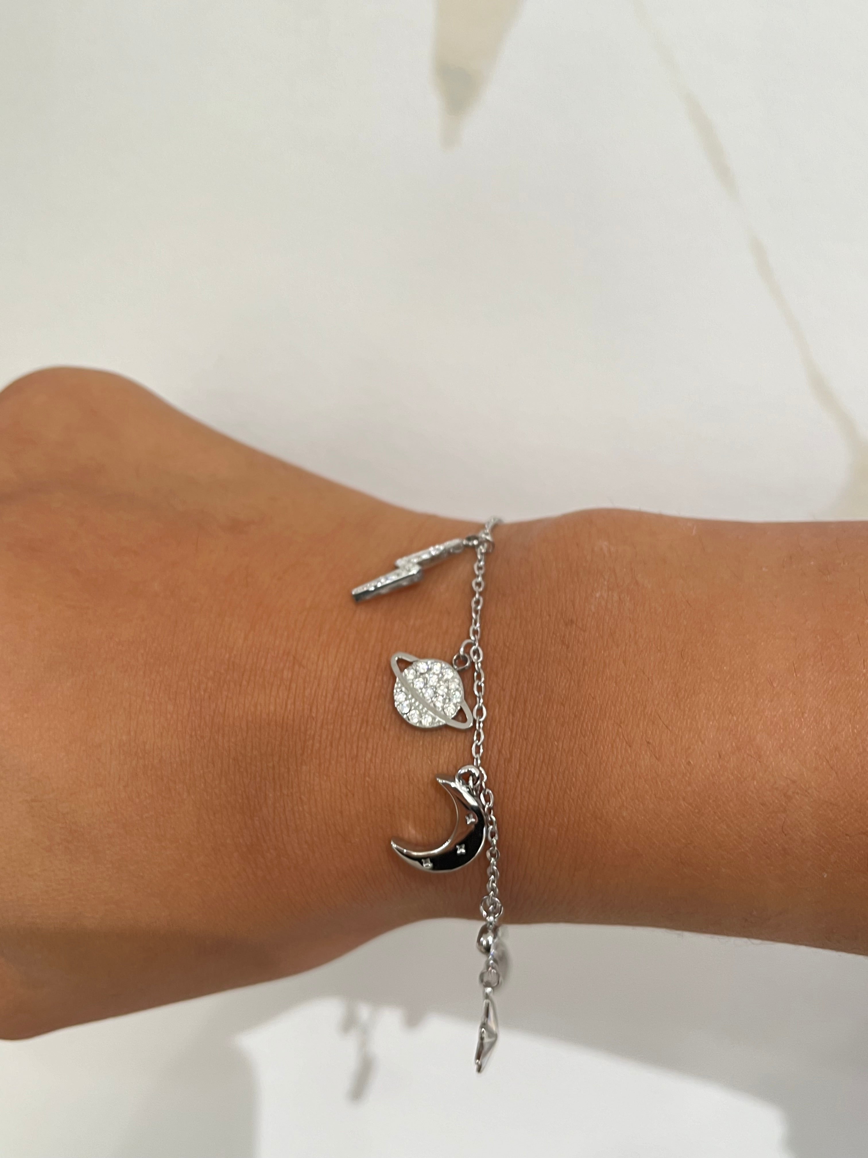Bracelet argent à maillons fins avec breloques en forme d'éclair, de lune et de planète.