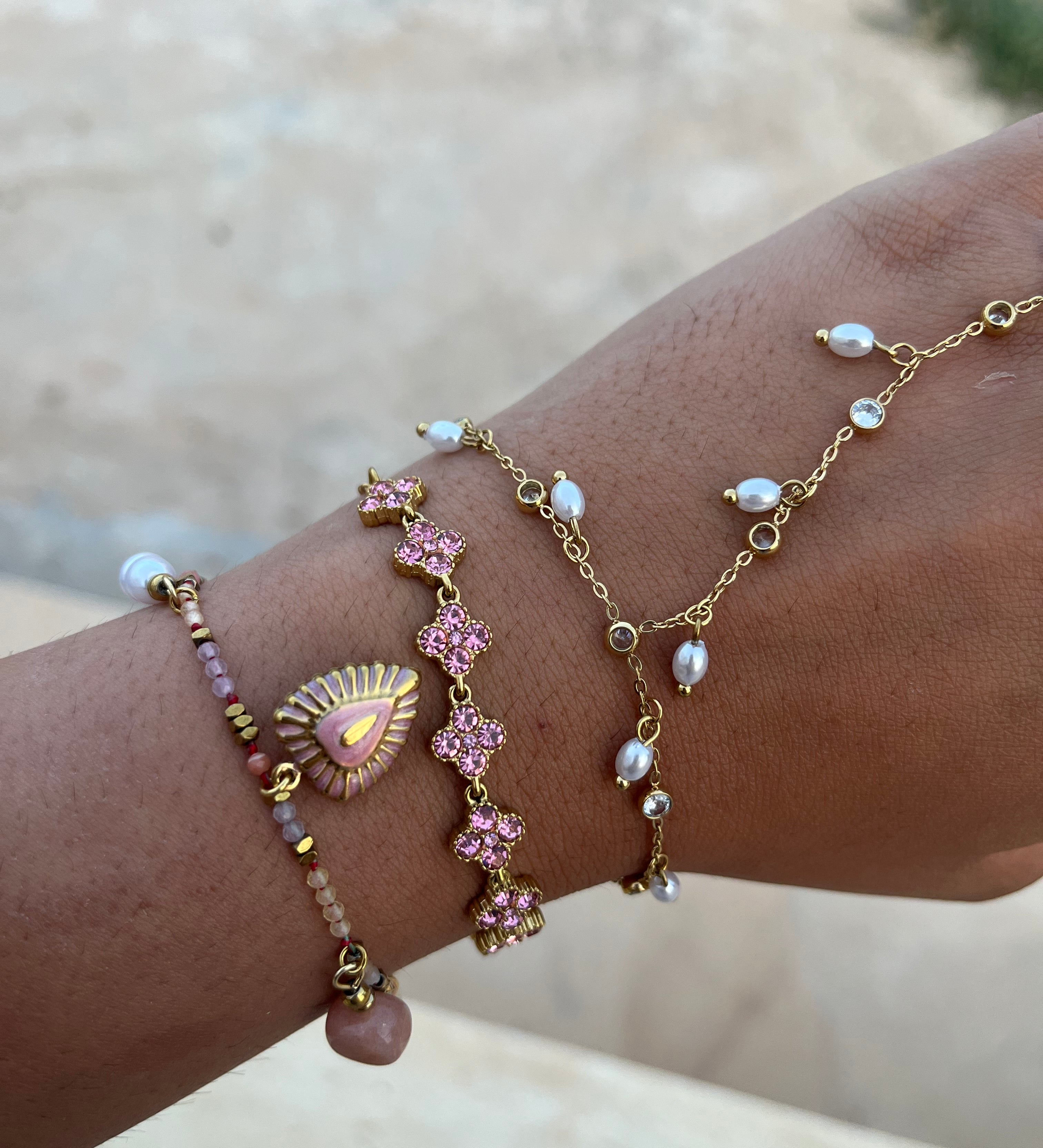 Accumulation de bracelets fins dorés au poignet mettant en valeur le bracelet Coraline en acier inoxydable aux pierres facettées roses - Ordiajade