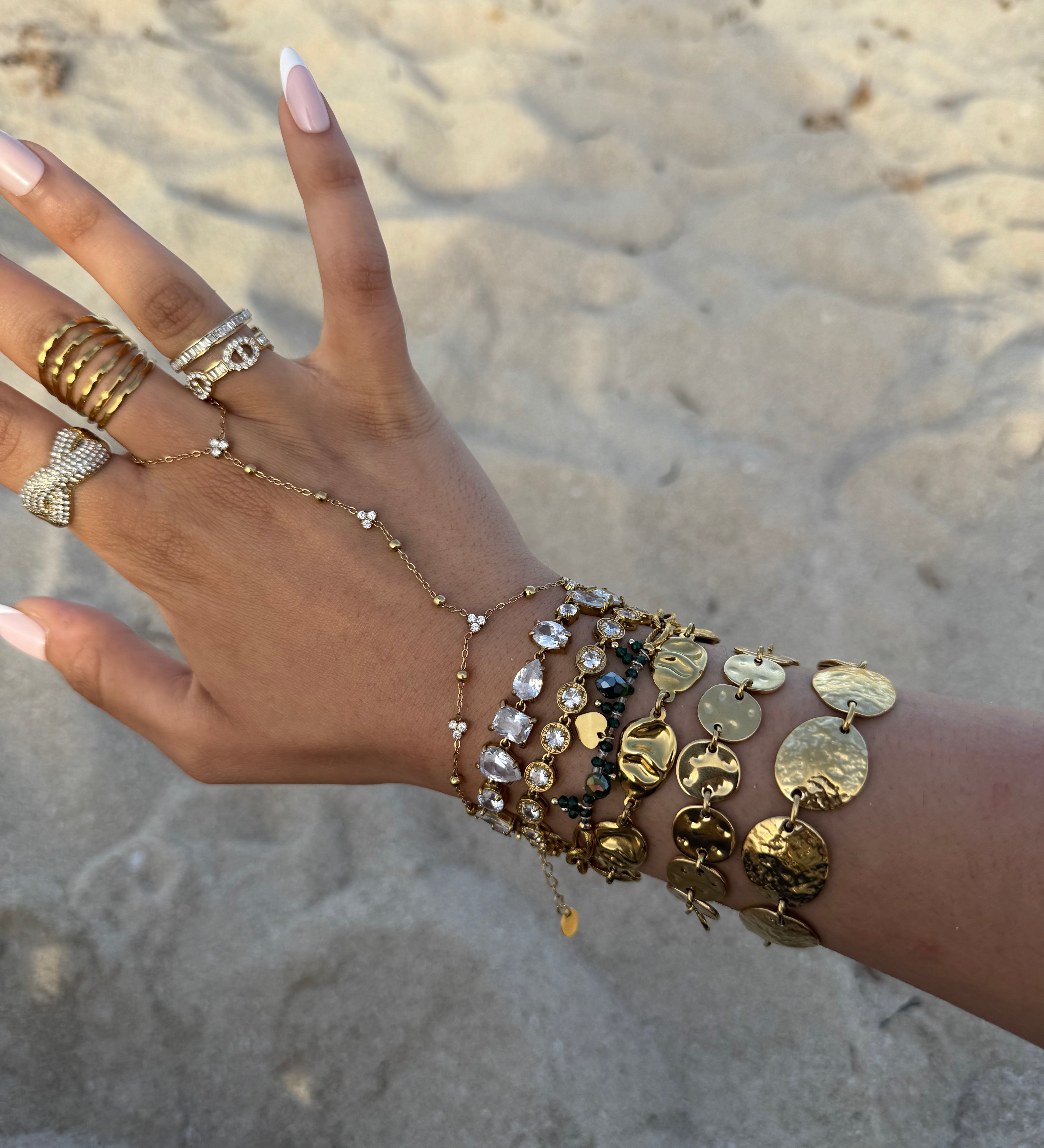 Bracelet doré Soug à maillons galbés porté en accumulation au poignet sur fond de sable - Ordiajade