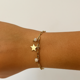 Bracelet Swanni doré en acier inoxydable avec pampilles étoile et perle porté au poignet.