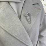 Broche Olympiade argentée en acier inoxydable maillons entrelacés avec chaînettes pendantes portée sur manteau - Ordiajade