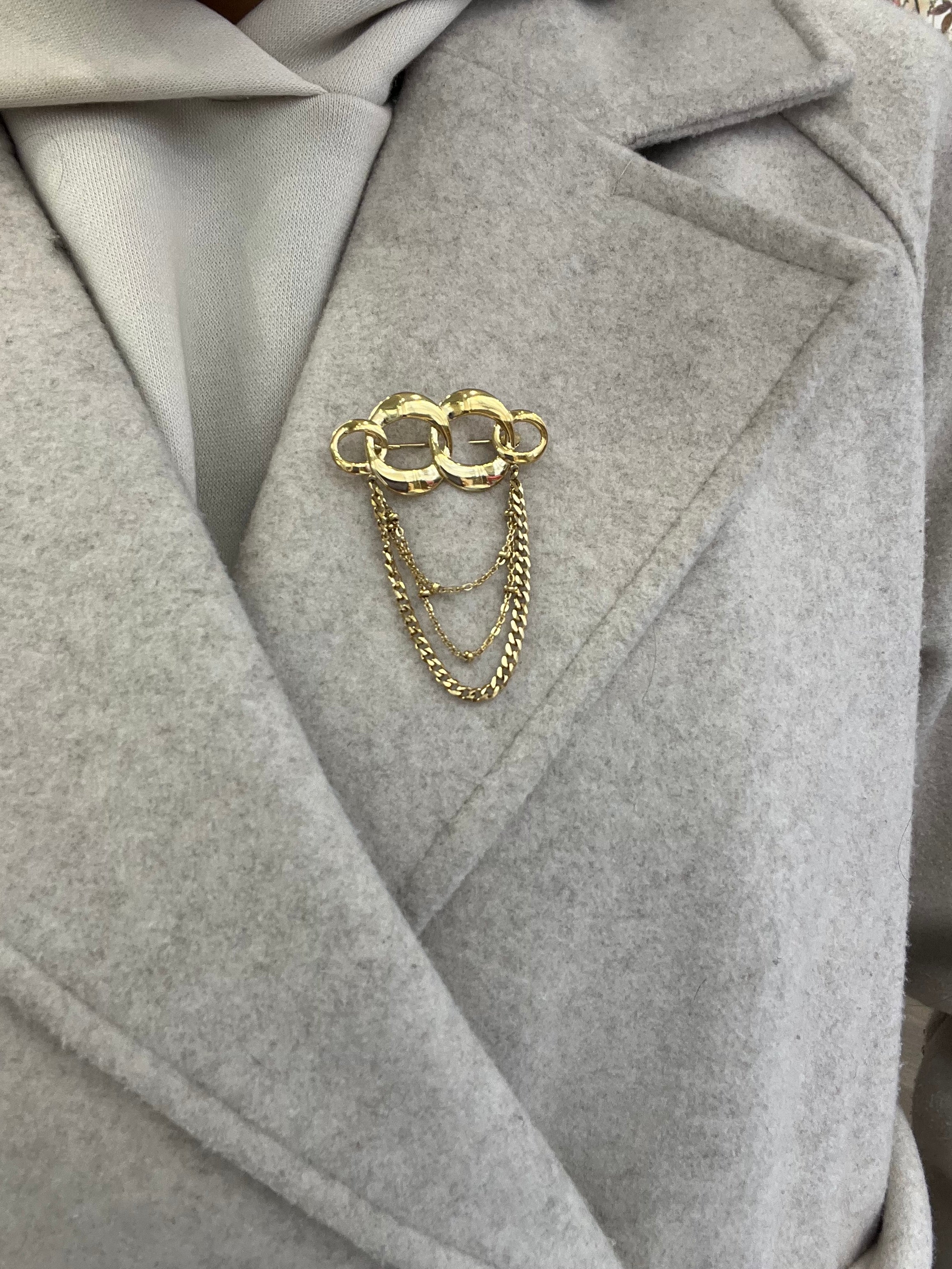 Broche Olympiade dorée en acier inoxydable maillons entrelacés avec chaînettes pendantes portée sur manteau - Ordiajade