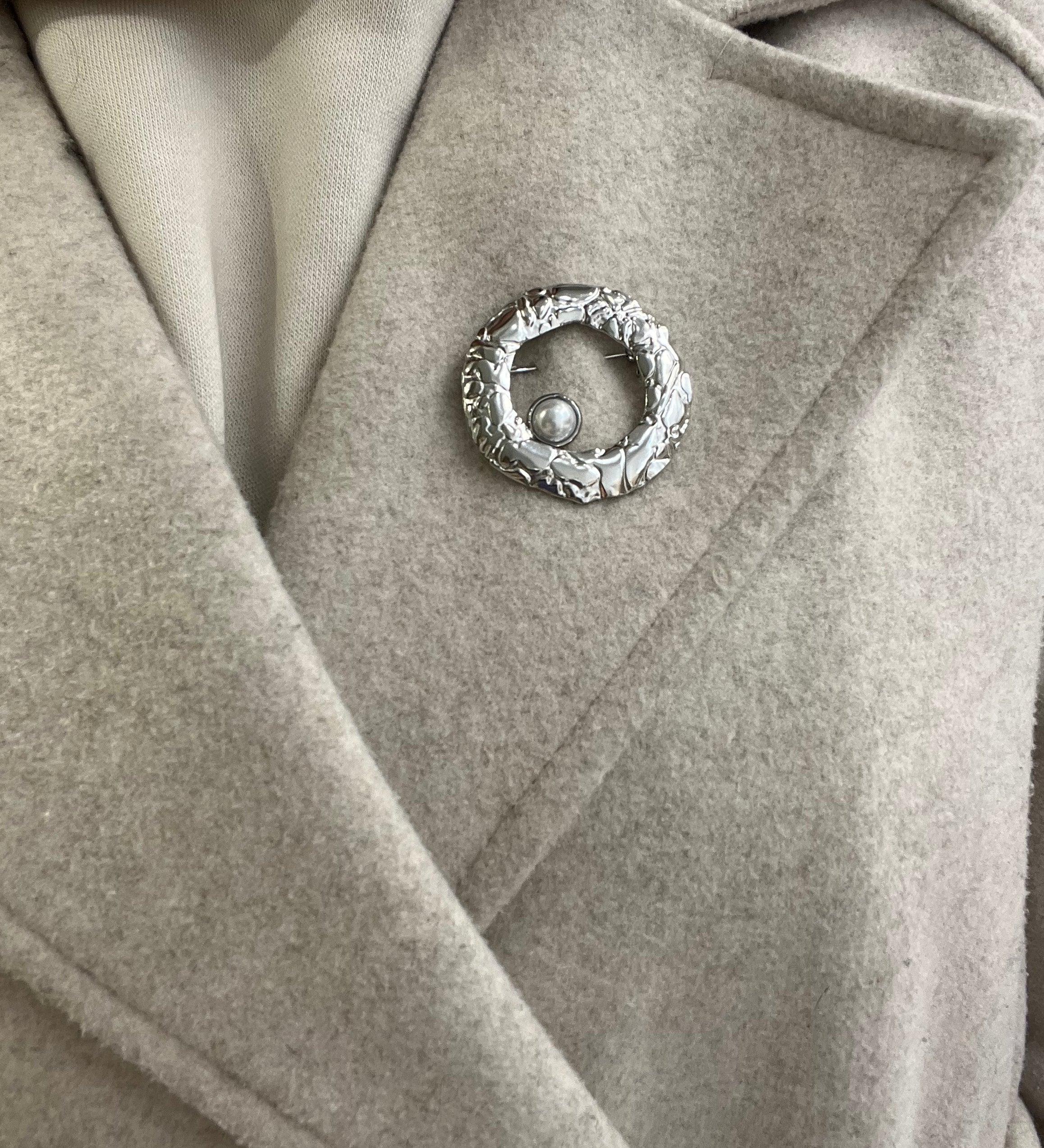 Broche Sylviane argentée en acier inoxydable anneau martelé avec perle portée sur le revers d'un manteau beige - Ordiajade