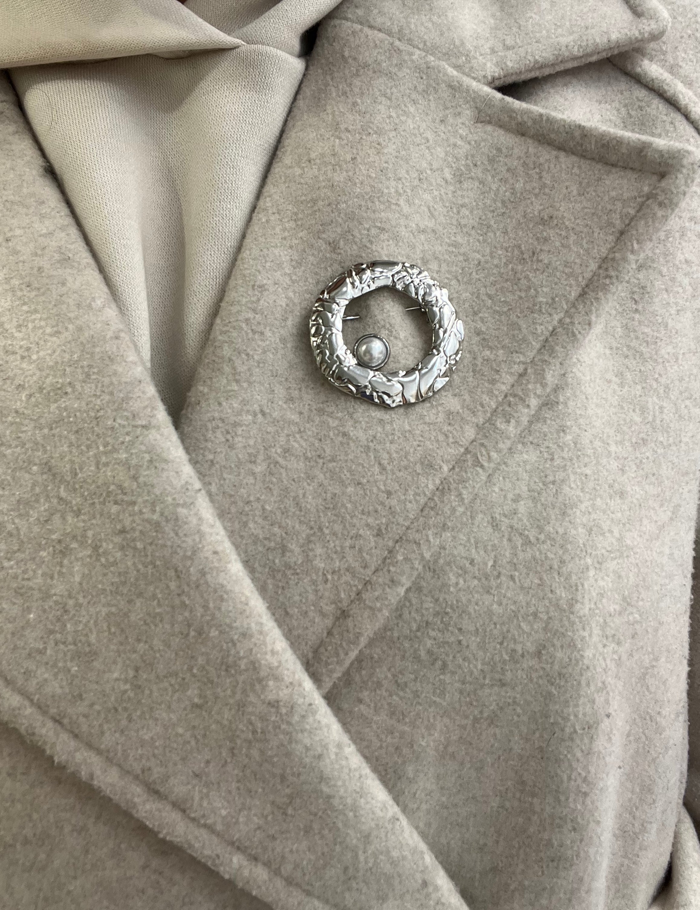 Broche Sylviane argentée en acier inoxydable anneau martelé avec perle portée sur le revers d'un manteau beige - Ordiajade