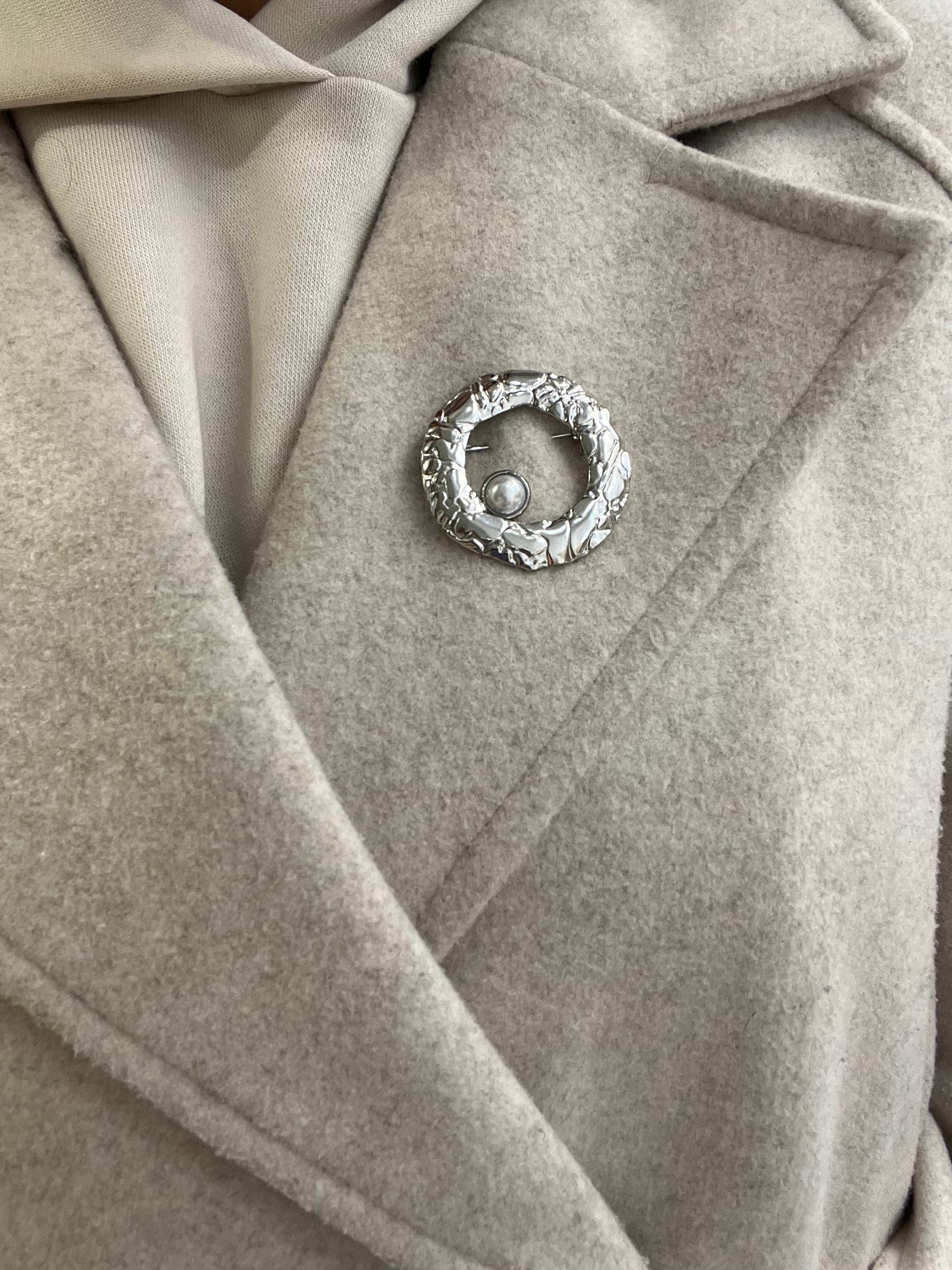Broche Sylviane argentée en acier inoxydable anneau martelé avec perle portée sur le revers d'un manteau beige - Ordiajade