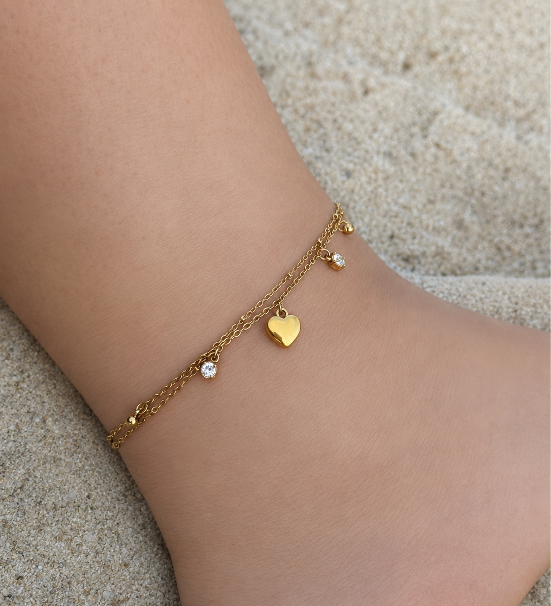 Chaîne de cheville double SHANA en acier inoxydable doré avec cœur et strass portée sur la plage - Ordiajade