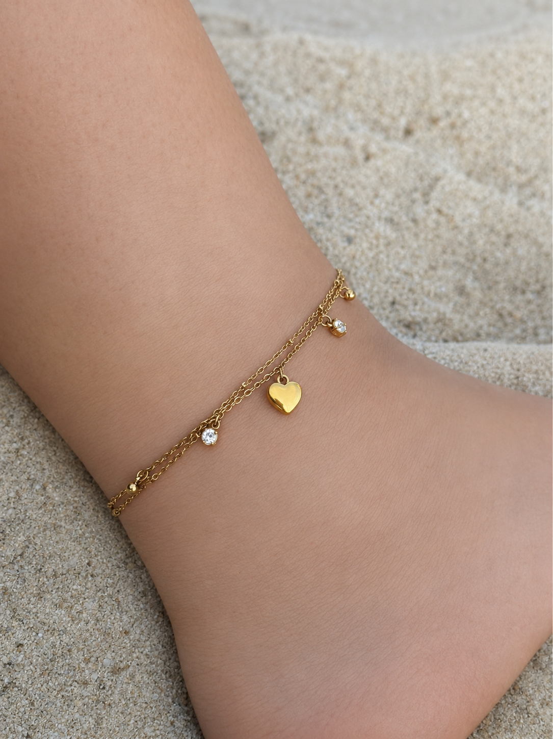 Chaîne de cheville double SHANA en acier inoxydable doré avec cœur et strass portée sur la plage - Ordiajade