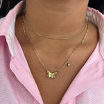 Collier double chaîne Austra doré avec pendentif papillon et zircon, porté sur une chemise rose.