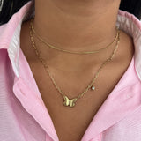 Collier double chaîne Austra doré avec pendentif papillon et zircon, porté sur une chemise rose.