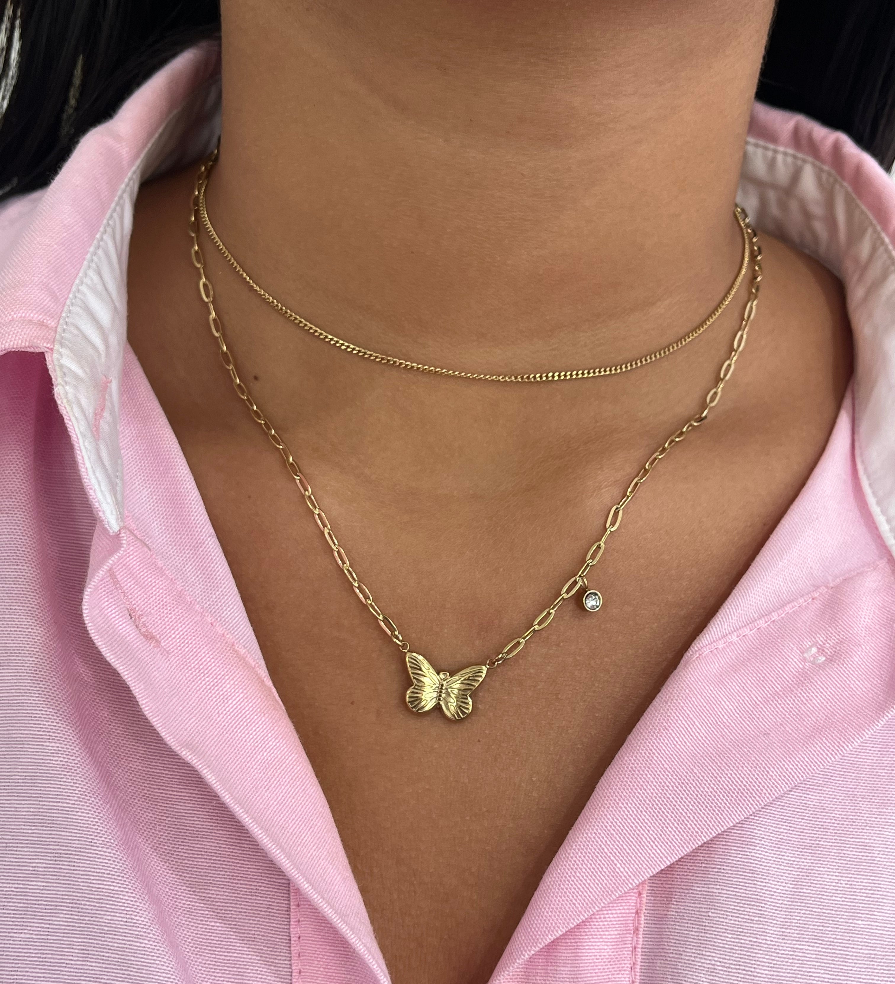 Collier double chaîne Austra doré avec pendentif papillon et zircon, porté sur une chemise rose.