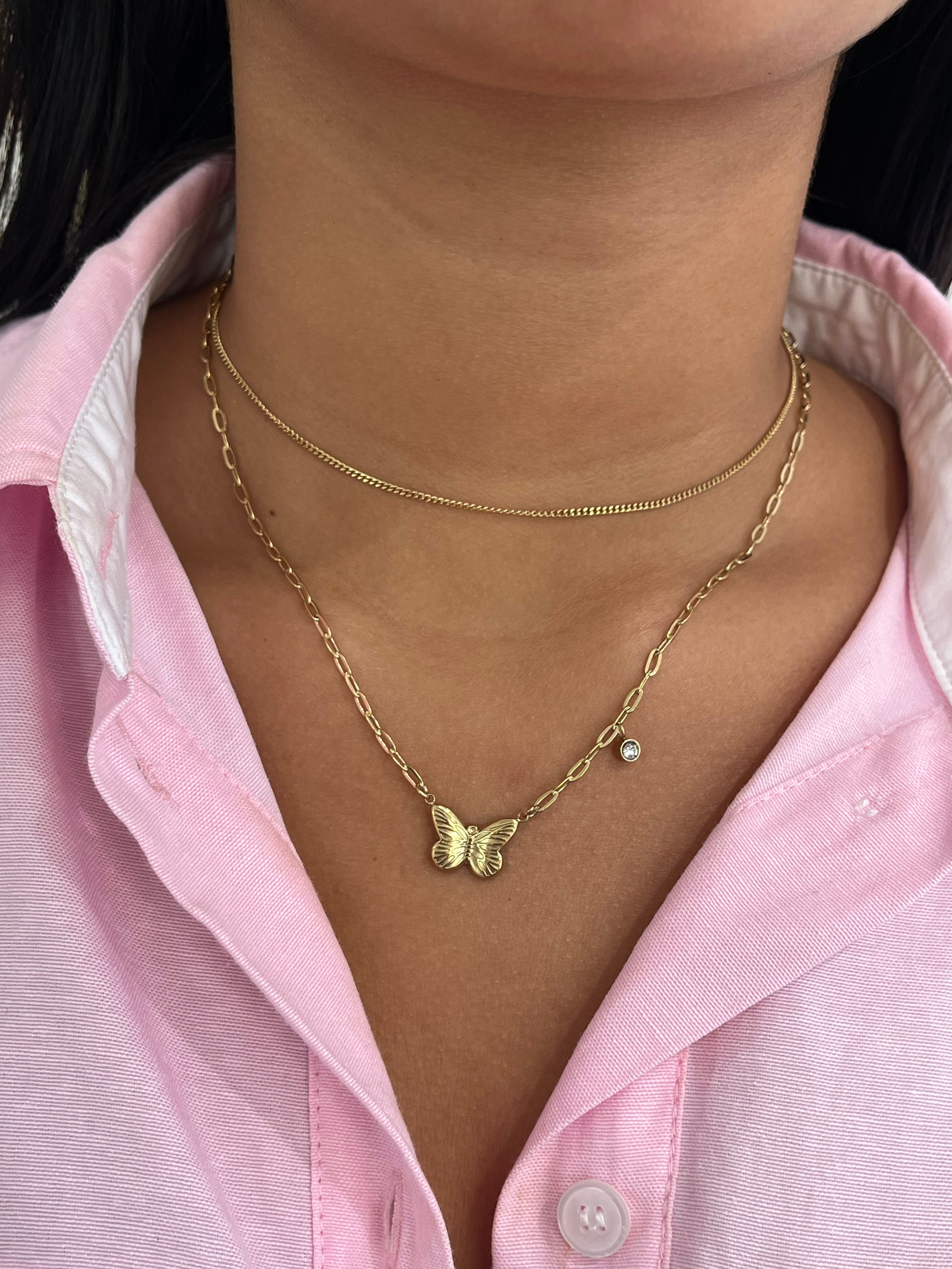 Collier double chaîne Austra doré avec pendentif papillon et zircon, porté sur une chemise rose.