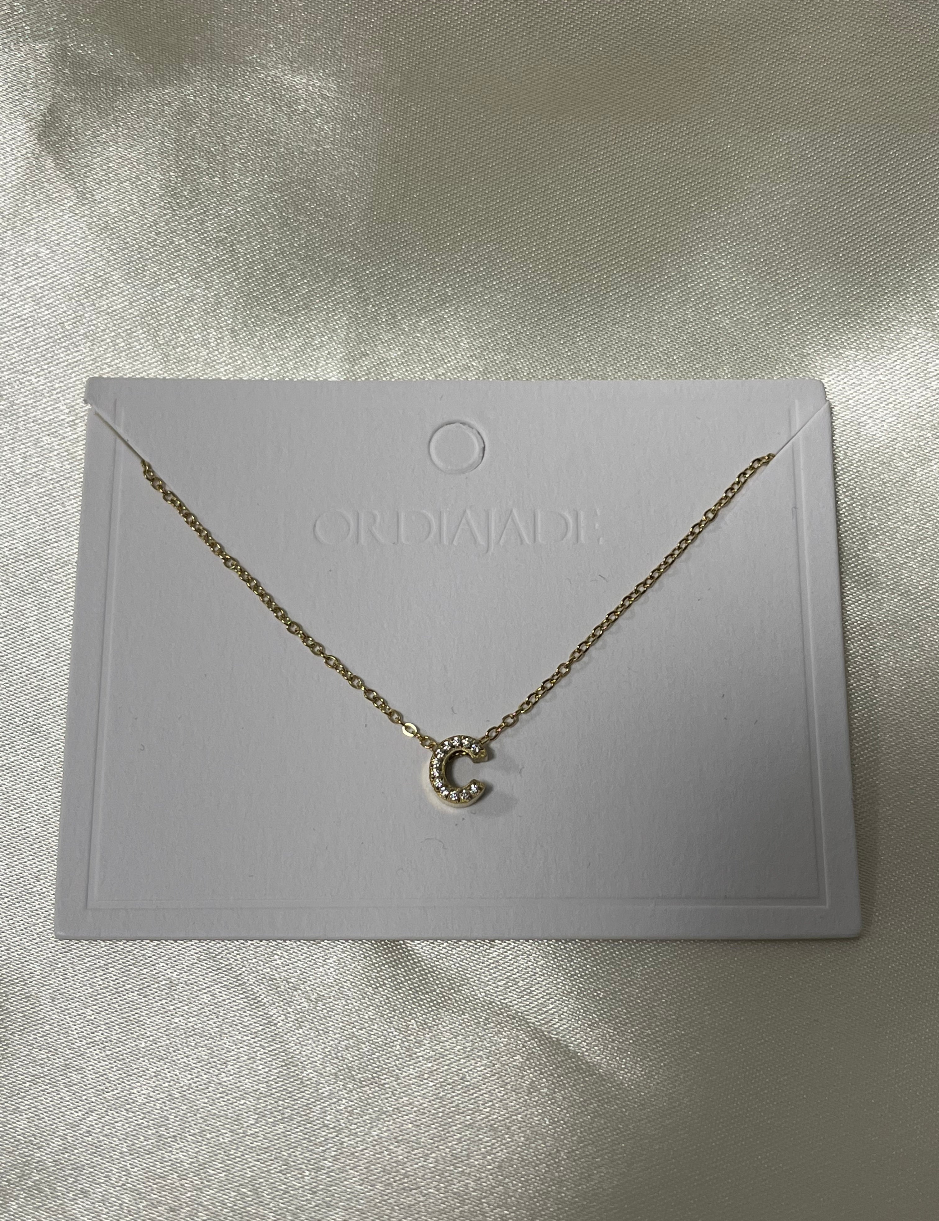 Collier Cuty doré à initiale C sertie de strass, sur sa carte de présentation - Ordiajade