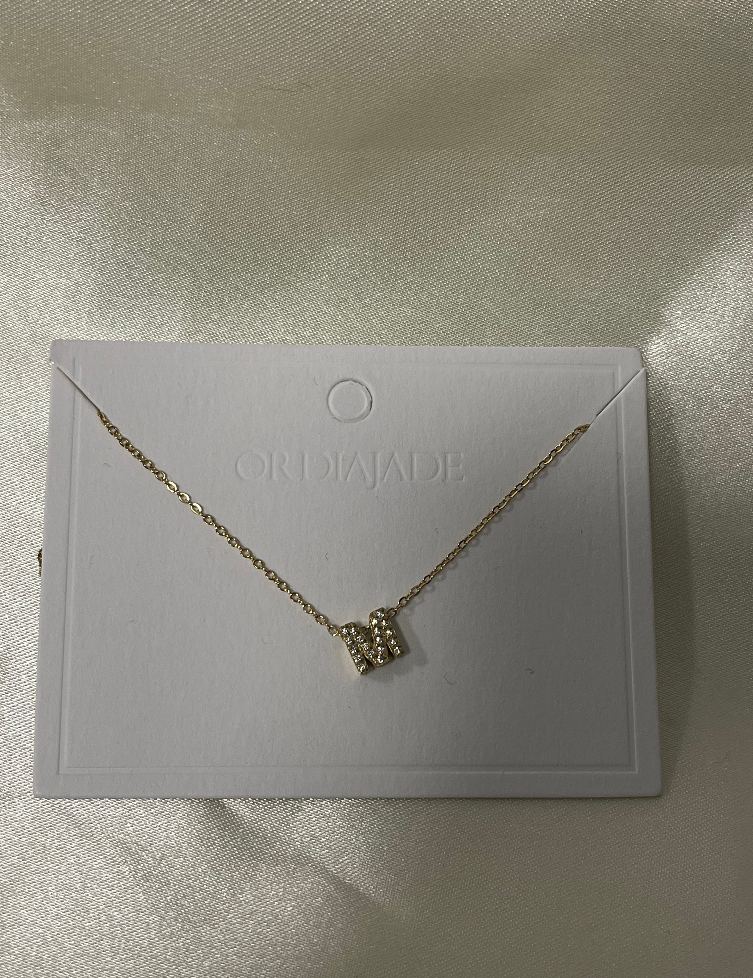 Collier Cuty doré à initiale M sertie de strass, sur sa carte de présentation - Ordiajade