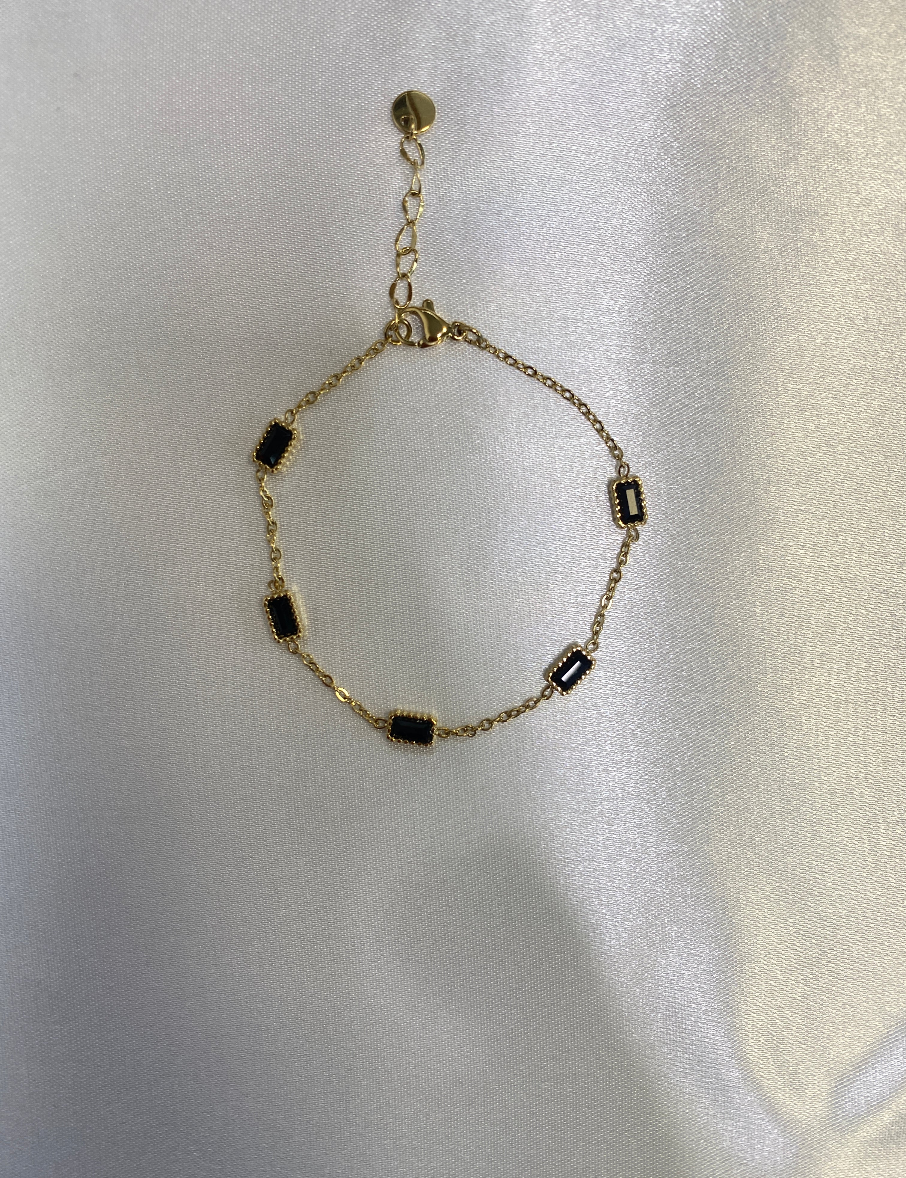 Bracelet Bloom doré à petites pierres noires serties, posé sur un satin - Ordiajade